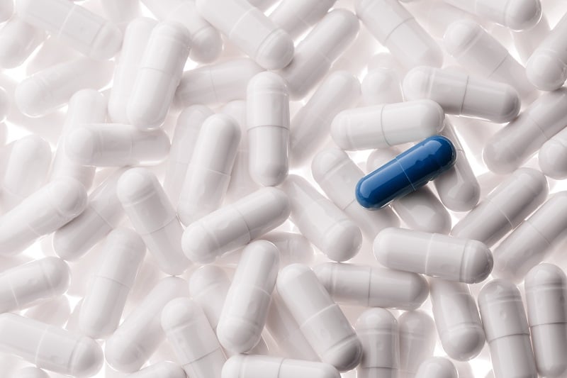 Image of many white pills with a single blue pill on top 
