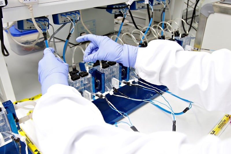 Image of a persons gloved hands working in a lab interacting with an experiment 