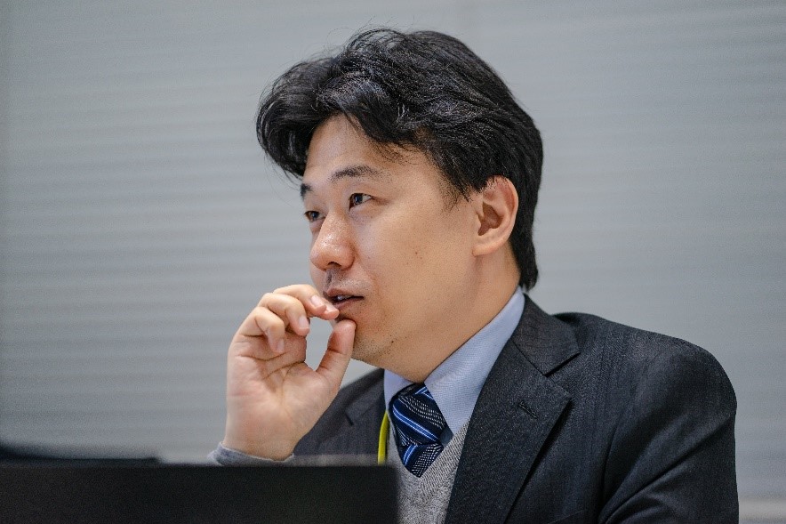 Male presenting person wearing a suit, in a contemplative pose with their hand to their chin