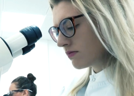 Image of a female presenting scientist looking into a microscope 